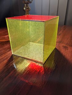 a green box sitting on top of a wooden table next to a light bulb and a lamp