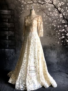 a dress on display in front of a tree with white flowers and branches behind it