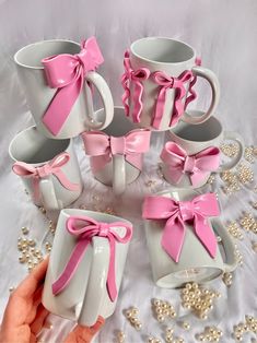 pink and white coffee mugs with bows on them are being held by someone's hand