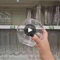 a hand holding a clear glass in front of shelves with empty water glasses on it