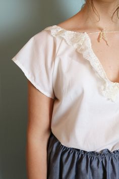 a woman wearing a white blouse and blue pants with a gold necklace on her neck