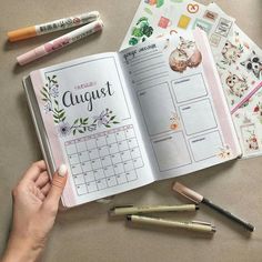 a person holding an open planner next to some crayons and pencils on a table