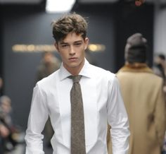 a young man in a white shirt and tie walks down the runway at a fashion show