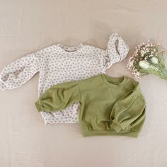 two baby sweaters laying on top of a bed next to a bouquet of flowers