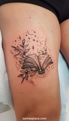 an open book tattoo on the side of a woman's thigh, with leaves and stars