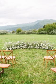 two wooden chairs sitting in the middle of a field with flowers on each side and mountains in the background