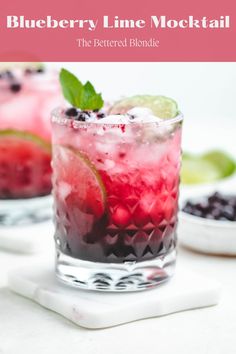 two glasses filled with blueberries and limeade on a white plate next to lemon wedges