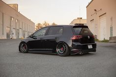 a black car parked in front of a building with red rims on it's tires