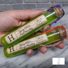 two green bottles with writing on them are being held by someone's hand