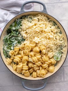 a pot filled with pasta and spinach on top of a white countertop next to a towel