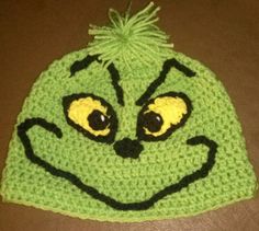 a crocheted hat with an angry grin face on the front and sides, sitting on a table