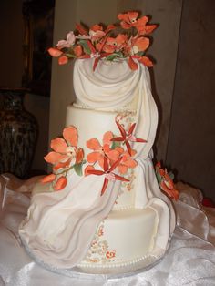 a three tiered wedding cake with orange flowers on the top and bottom, sitting on a white table cloth