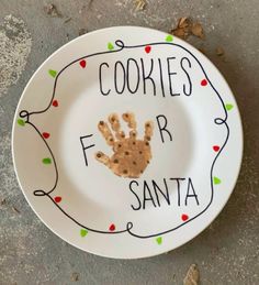 a plate with a handprint on it that says cookies for santa and is decorated with christmas lights