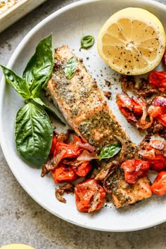 a white plate topped with salmon, tomatoes and spinach next to a lemon wedge