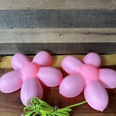 three pink plastic flowers sitting on top of a wooden table next to a green plant