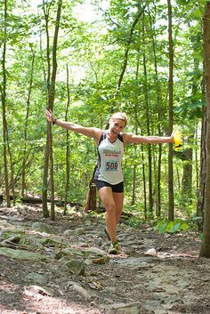 a woman is running through the woods with her arms outstretched