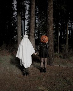 two people dressed up as ghost and pumpkins walking through the woods with their hands in each other's pockets