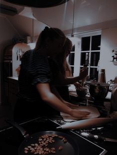 two women in the kitchen preparing food on an electric stove top burner and frying pans