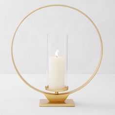 a white candle in a glass holder with a gold stand on a white table top