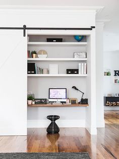 a computer desk sitting in front of a white book shelf filled with books and other items