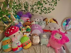 a pile of stuffed animals sitting on top of a bed next to a green plant