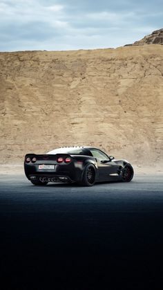 the black sports car is parked in front of a mountain and sand hill side area