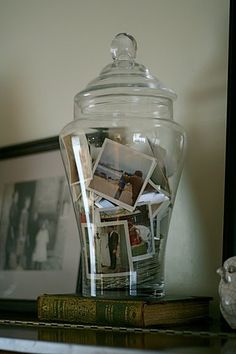 a glass jar filled with pictures sitting on top of a table next to a book