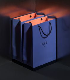 two blue shopping bags sitting on top of each other in front of a black wall