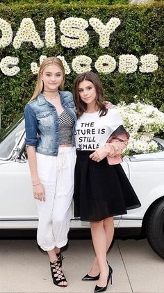 two women standing in front of a white car