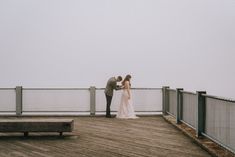 a bride and groom standing on a pier