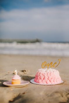 a pink and white cake sitting on top of a sandy beach