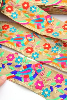 someone is holding up some colorful ribbon with flowers on it and another piece of fabric in the background