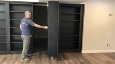 a man standing in front of an open bookcase with his hand on the door