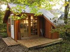 a small wooden cabin in the woods surrounded by trees and leaves, with its door open