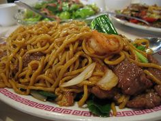 a plate filled with noodles and meat on top of a table next to other plates