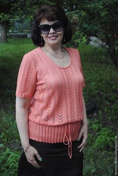 a woman wearing sunglasses standing in front of some trees and grass with her hands on her hips