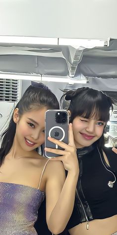 two young women taking a selfie in front of a mirror with headphones on