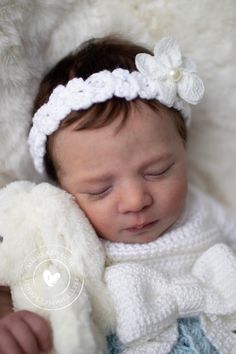 a baby wearing a crochet headband laying on top of a white blanket