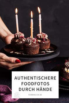 chocolate cupcakes with white frosting and lit candles in front of them on a black platter