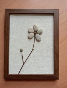 a frame with some rocks and a flower in it on a wooden table next to a wall