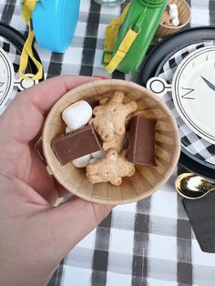 a person holding a small wooden bowl filled with chocolates and marshmallows