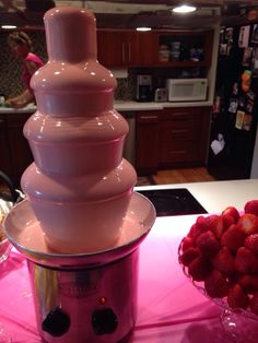 a chocolate fountain with strawberries in front of it on a pink tableclothed kitchen