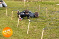 two people laying on the ground in front of several wooden poles with ropes attached to them