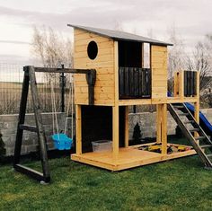 a wooden play house with a slide and swing set in the back yard on grass