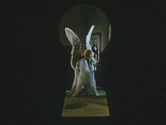 an angel is standing in the dark with its wings spread out and two people are looking at it