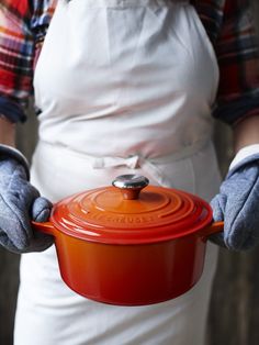 a person wearing gloves holding an orange casserole in one hand and two hands on the other