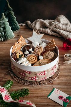 a christmas cookie tin filled with cookies and other holiday treats on a wooden table next to a tree