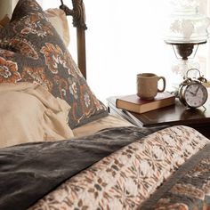 a coffee cup on a table next to a bed with pillows and blankets in front of a window