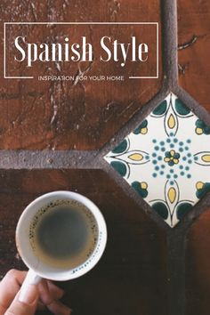 a person holding a cup of coffee in front of a tile wall with the words spanish style on it