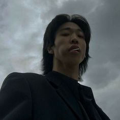 a young man is standing in front of a cloudy sky with his mouth open and toothbrush in his mouth